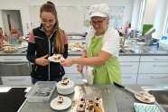Zwei Frauen stehen in der Schulküche und halten Kuchen in den Händen