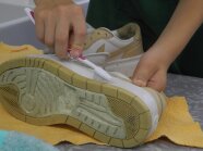 Hand hält alte Zahnbürste und putzt weißen Turnschuh