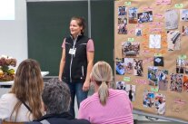 Frau steht vor Publikum im Klassenzimmer und hält einen Vortrag
