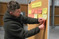 Mann steht an einem Flipchart und heftet einen Zettel an