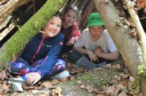 Drei Kinder sitzen in einer Höhle aus Ästen